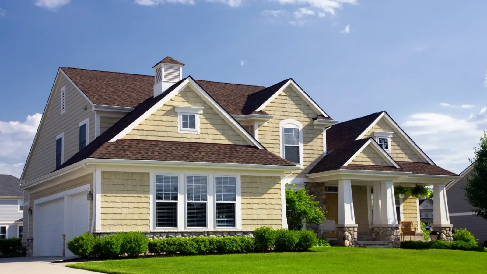 A two-story craftsman-style home with shingle siding, a stone-trimmed front porch, and a manicured lawn